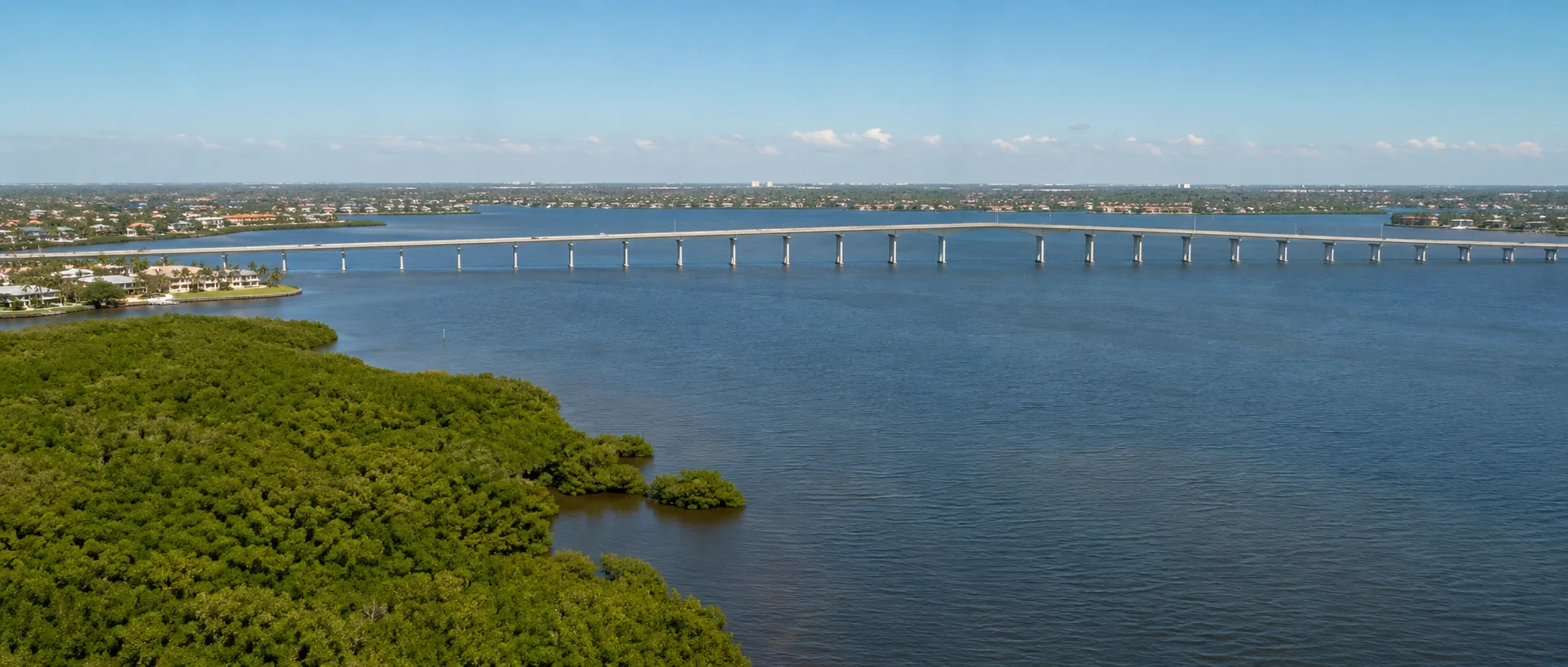 Mangrove shoreline, river and a fixed-span bridge representing the Four Mile Cove and Midpoint Bridge area of Cape Coral.