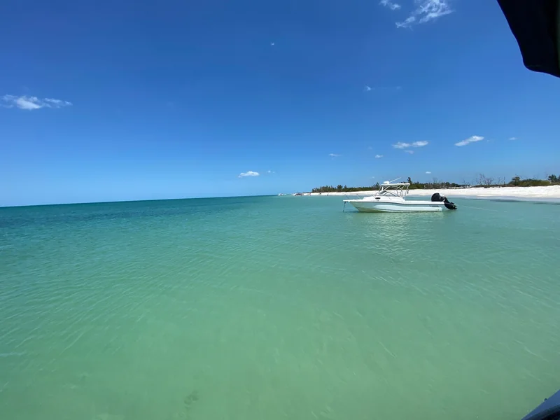 Boat anchored in shallow turquoise water beside a white sandy beach