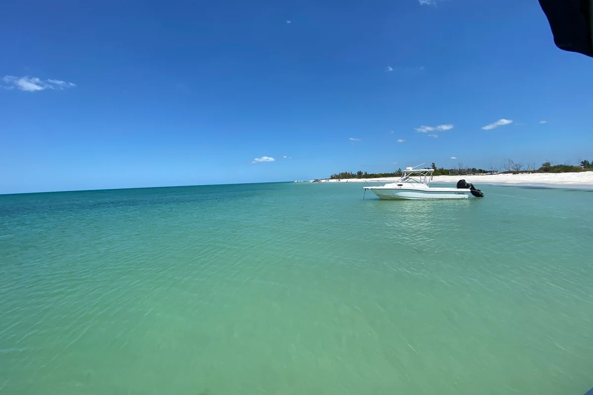 Boat anchored in shallow turquoise water beside a white sandy beach, part of the Southwest Florida boating lifestyle