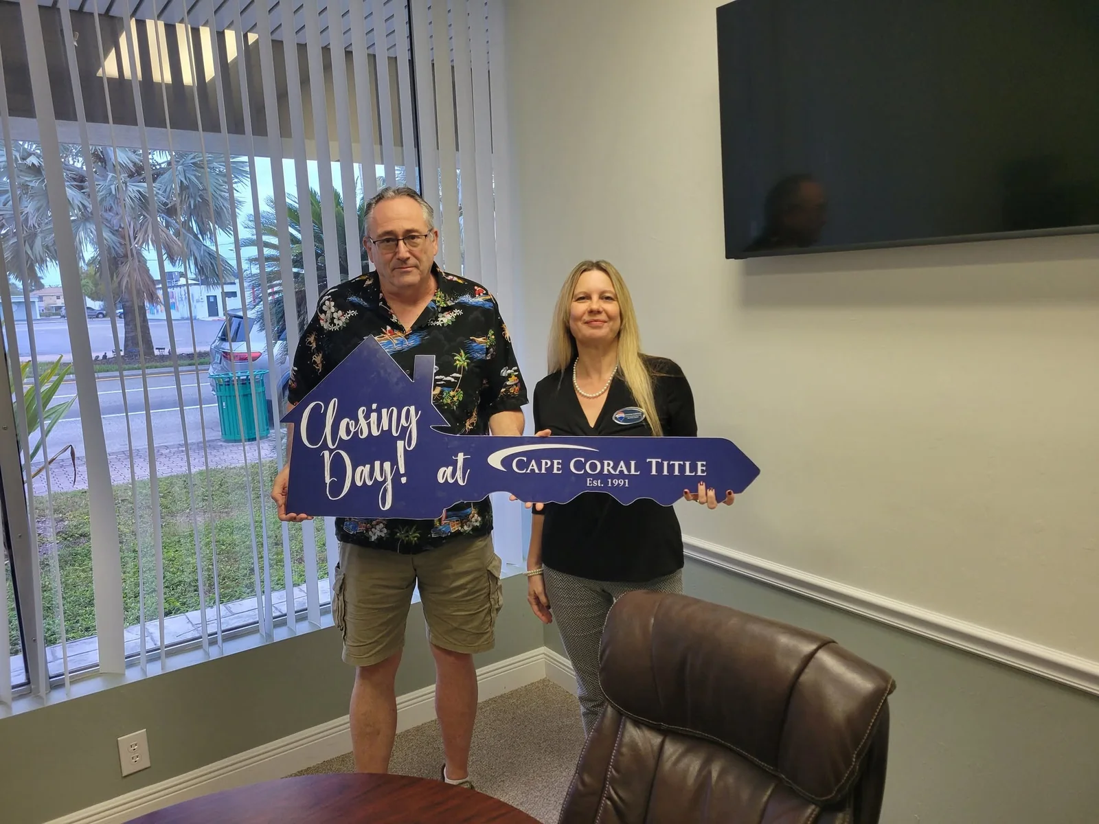 Christina Kalkmann with a client holding a Closing Day key at a Cape Coral title office.